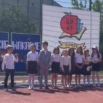 Na boisku szkolnym stoi 11 uczniów. W tle, z lewej strony dekoracja "WITAJCIE WAKACJE", z prawej strony, na płocie zawieszony baner z logo szkoły SP