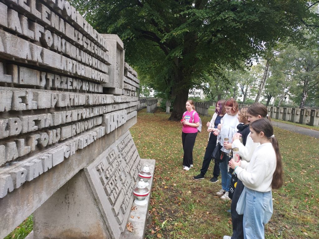 Sześć dziewczynek z klasy 7b stoi przed pomnikiem i trzyma w rękach znicze