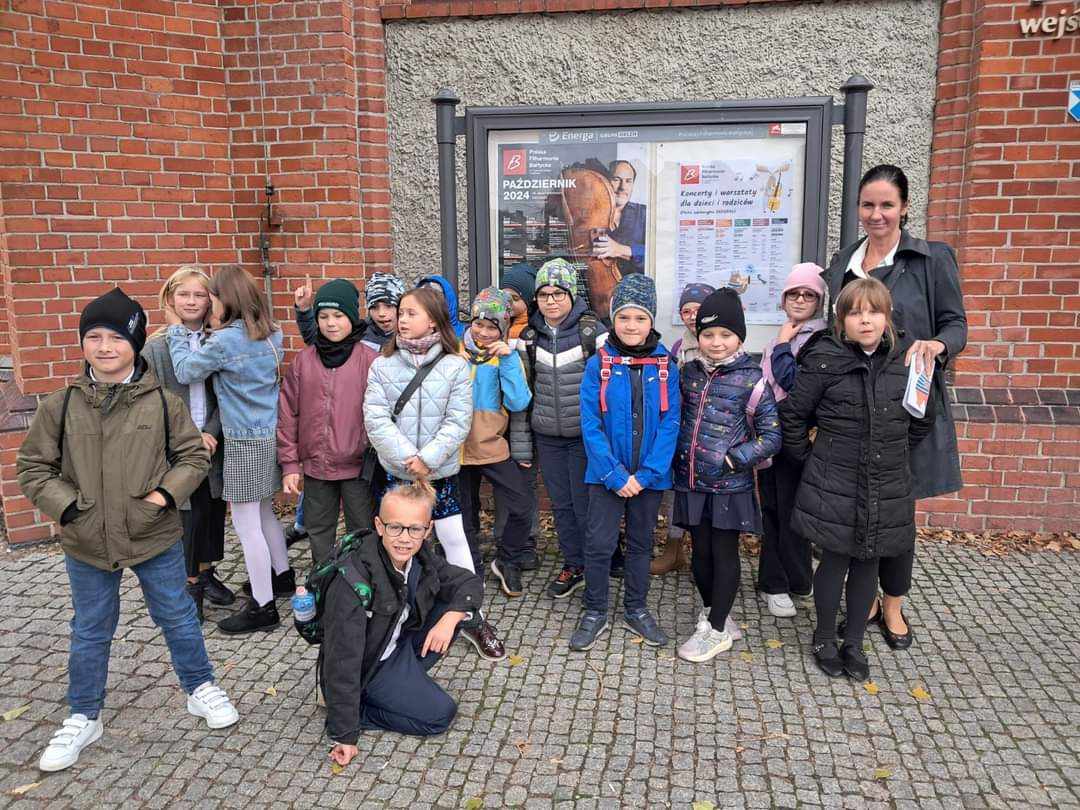 Około 15 uczniów stoi, z prawej strony wychowawczyni. 1 chłopiec klęczy przed grupą.