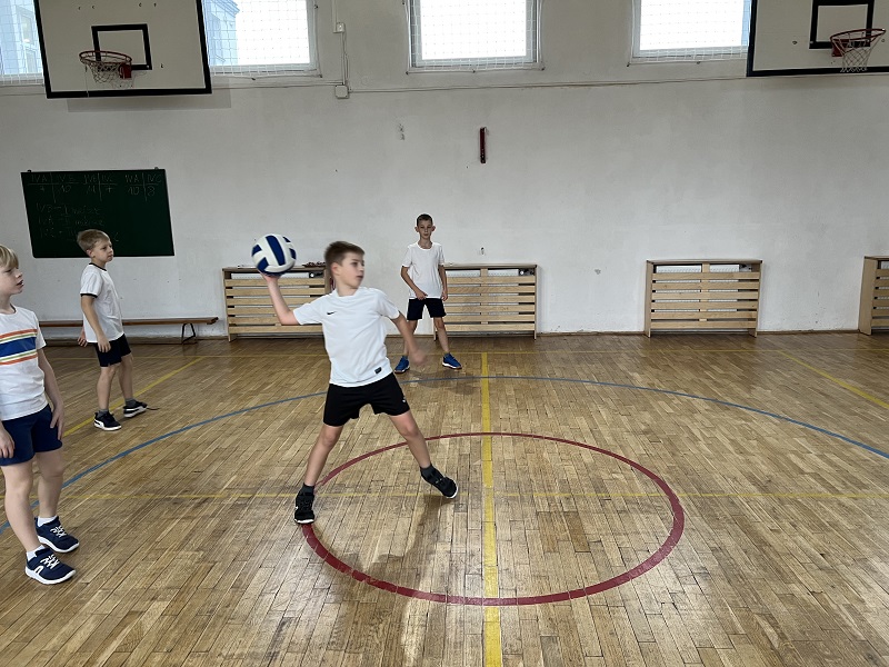 Uczeń z piłka wykonuje zamach do rzutu. Za nim 3 uczniów obserwuje jego próbę