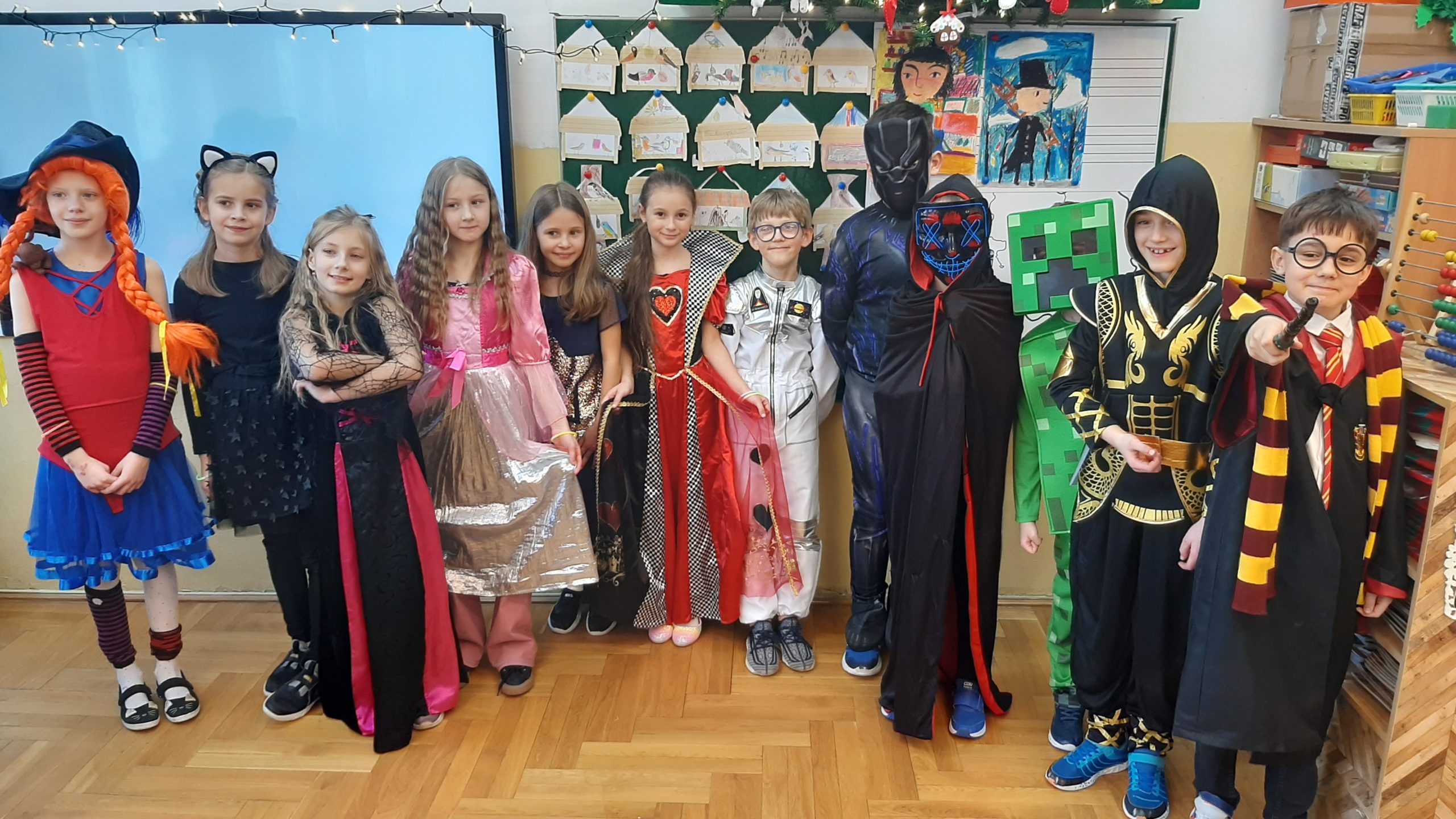12 uczniów w strojach karnawałowych stoi w swojej klasie.