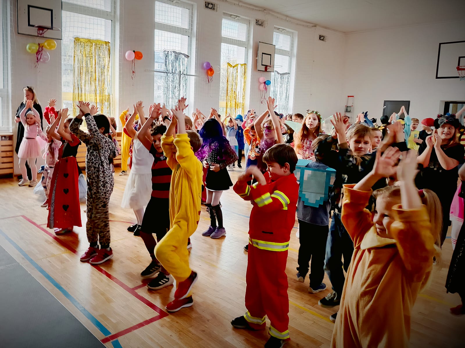 Dzieci w różnorodnych przebraniach karnawałowych stoją z uniesionymi rękami,