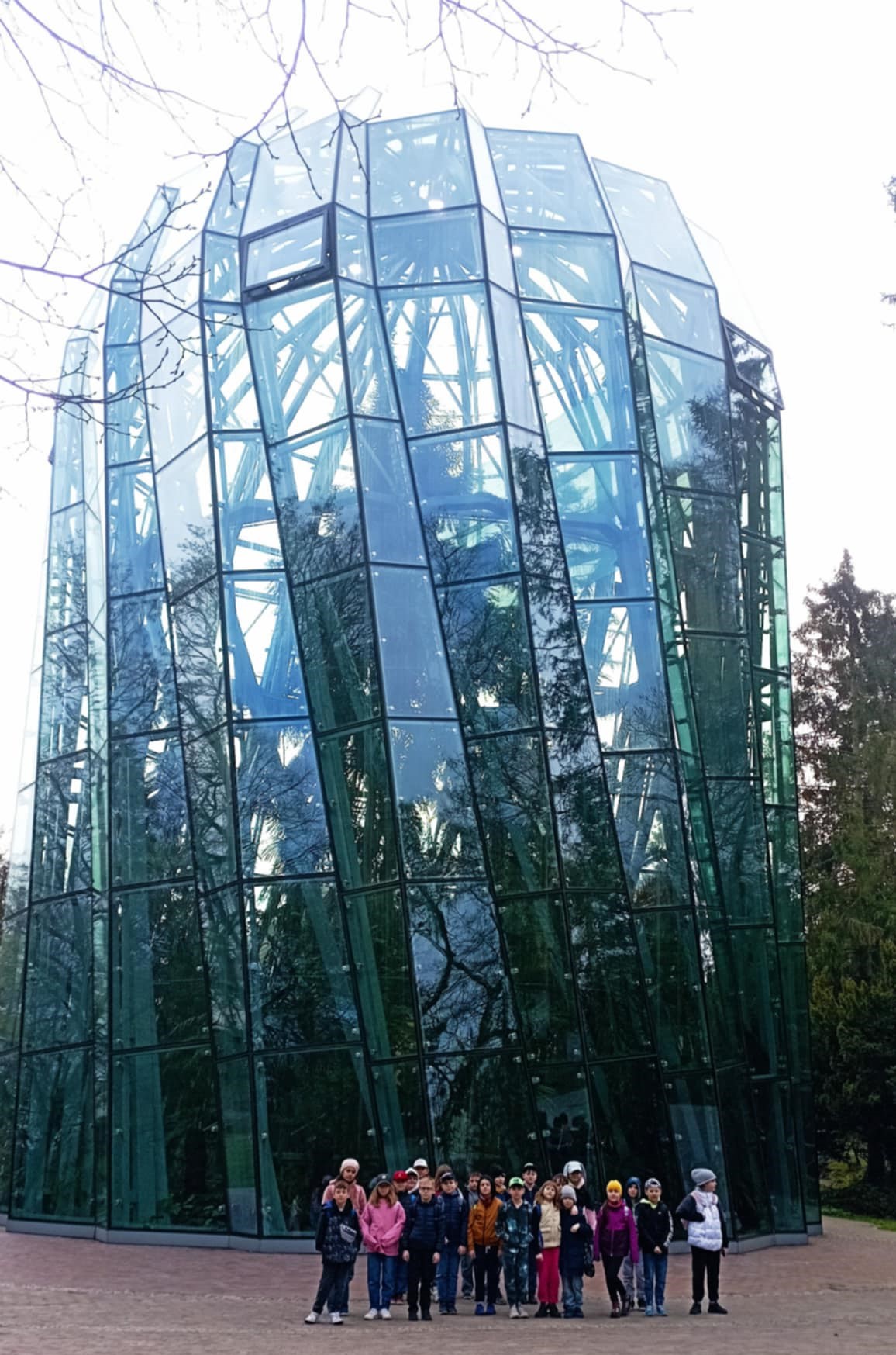Na tle oszklonego budynku Palmiarni w Parku Oliwskim stoi grupa uczniów klasy 3c.