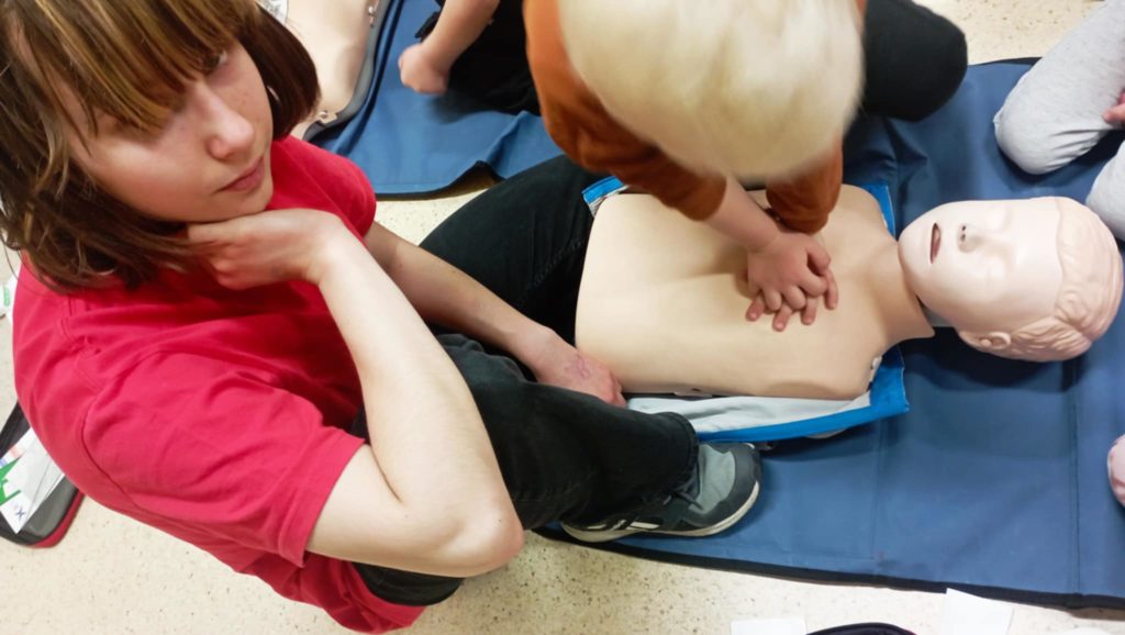 Na pierwszym planie przedszkolak uciskający klatkę piersiową fantoma. Obok uczennica Koła HOPR.