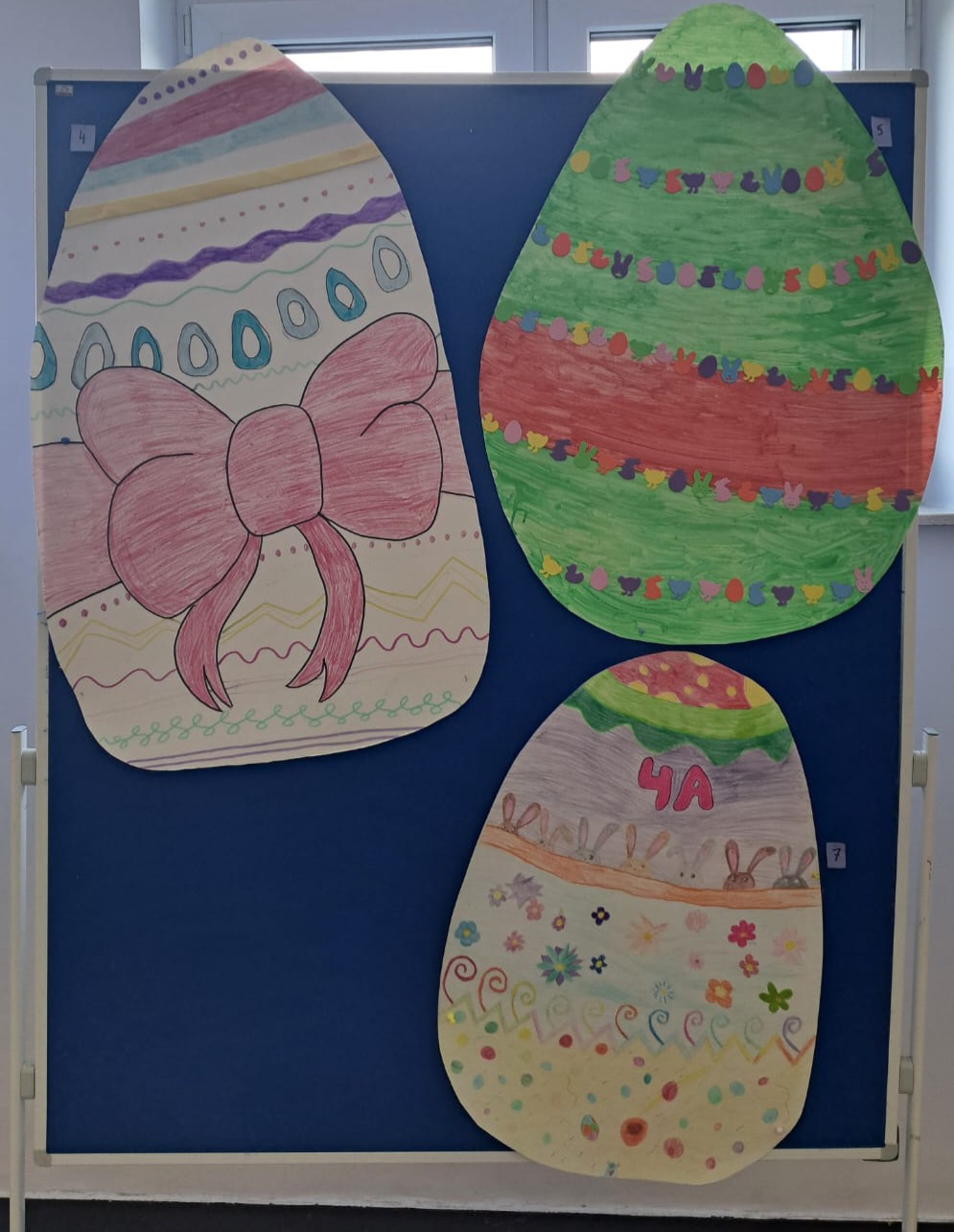 Widoczne 3 duże ozdobne jajka wielkanocne wykonane z papieru, umieszczone na tablicy.
