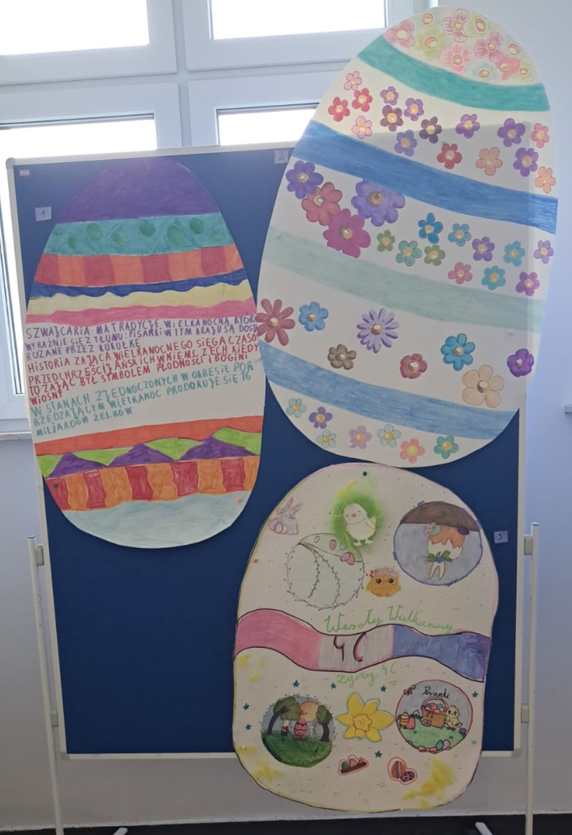 Widoczne 3 duże ozdobne jajka wielkanocne wykonane z papieru, umieszczone na tablicy.