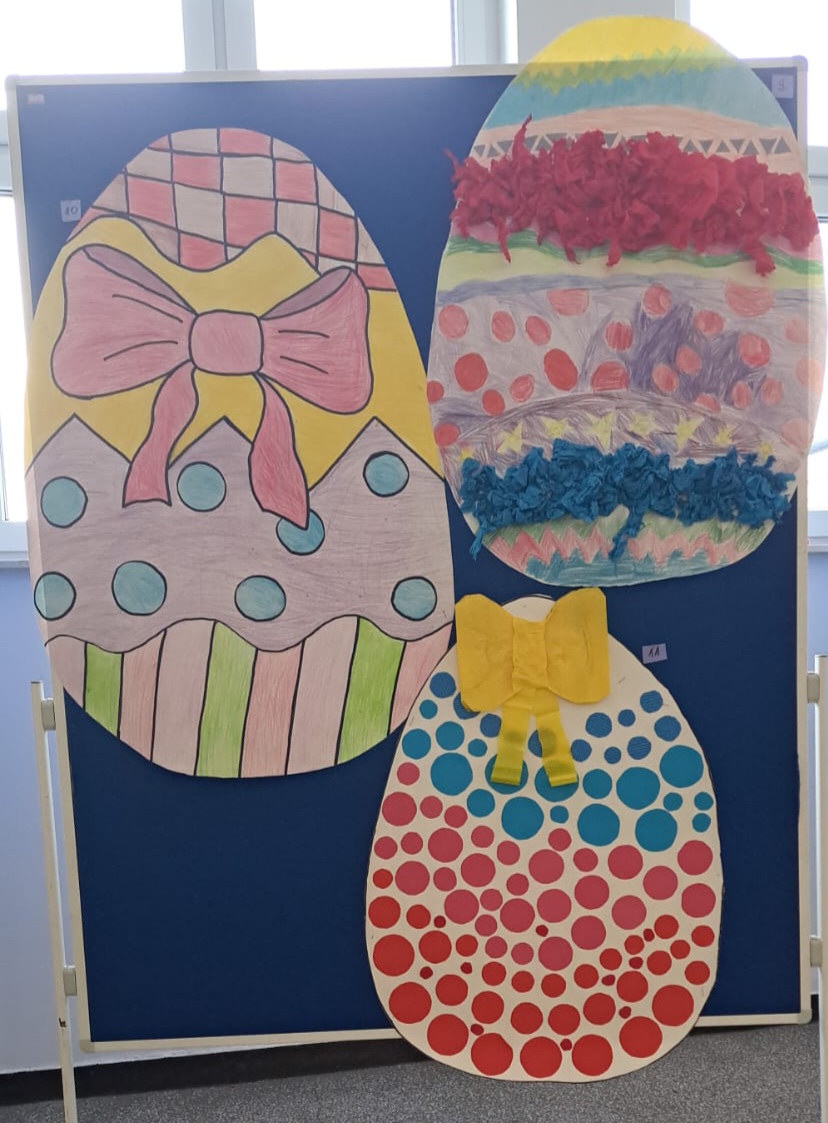 Widoczne 3 duże ozdobne jajka wielkanocne wykonane z papieru, umieszczone na tablicy.