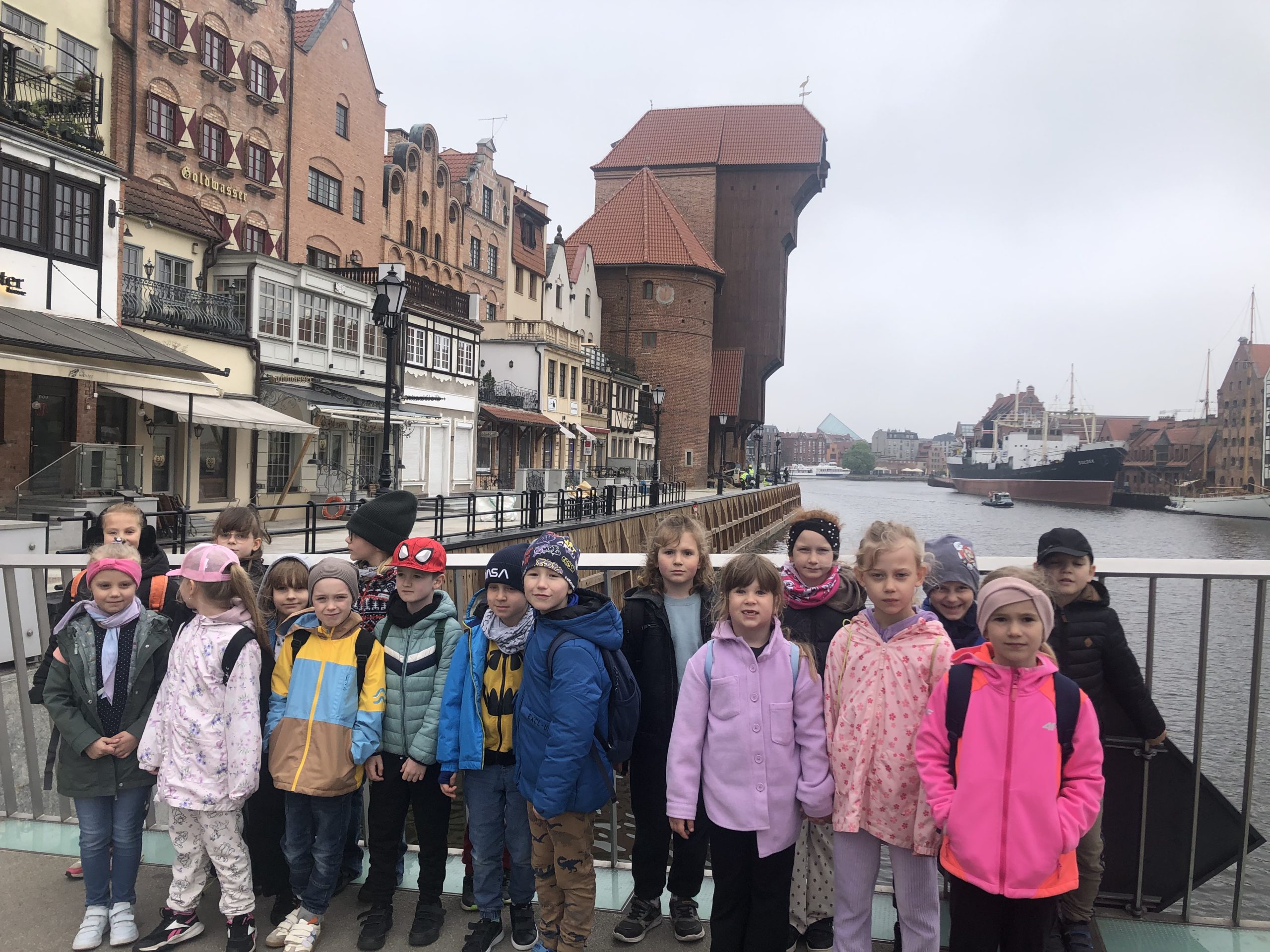 Grupa 18 dzieci stoi na kładce w tle prezentuje się budynek Żurawia
