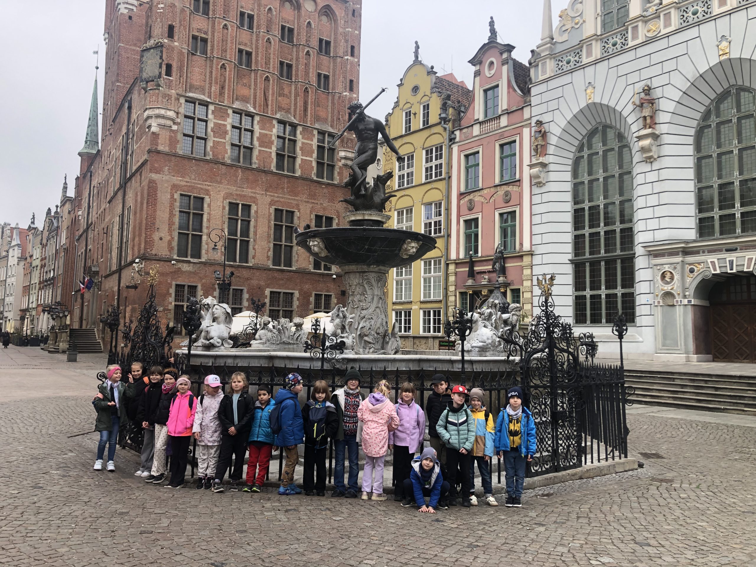 18 dzieci stoi przed fontanną Neptuna.
