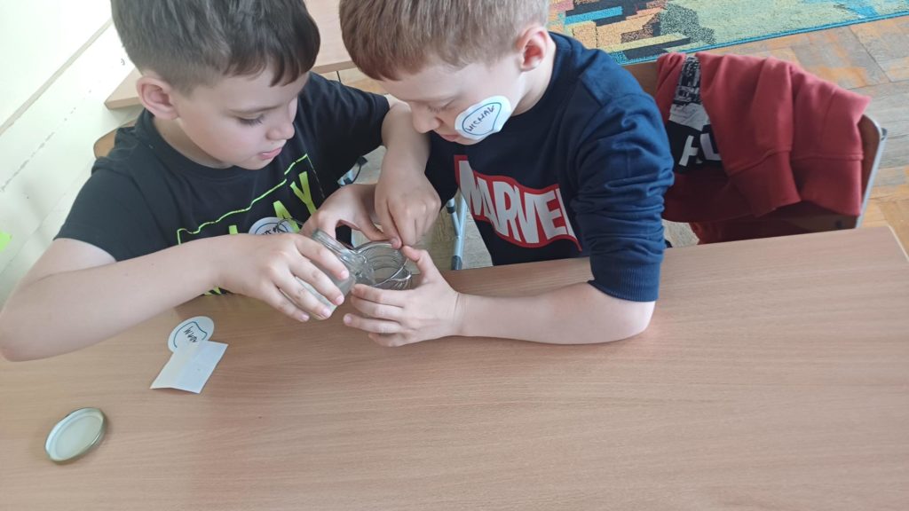 2chłopców siedzi w ławce i przelewała wodę ze słoika