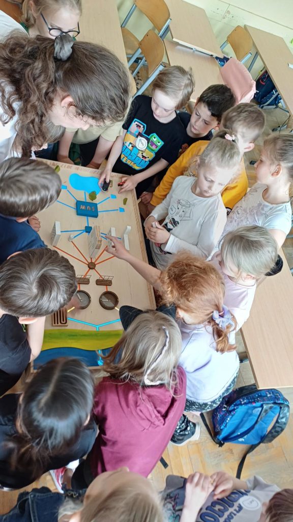 grupa dzieci stoi nad drewnianą makietą oczyszczalni ścieków 