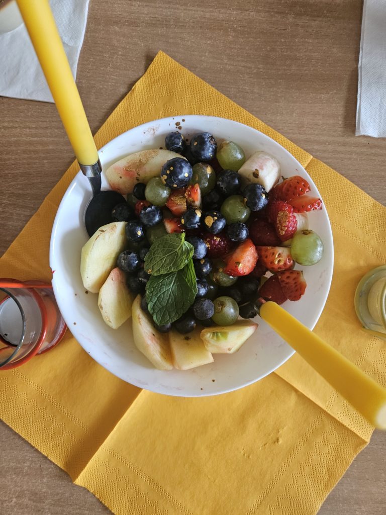 Sałatka owocowa z borówkami i truskawkami w miseczce, z żółtymi sztućcami.