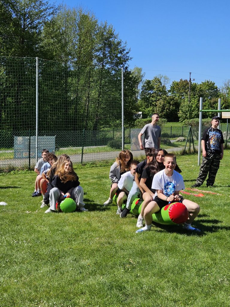 Na zdjęciu, na zielonej trawie dwa rzędy gumowych, kolorowych "gąsienic", na których podskakują zawodnicy.