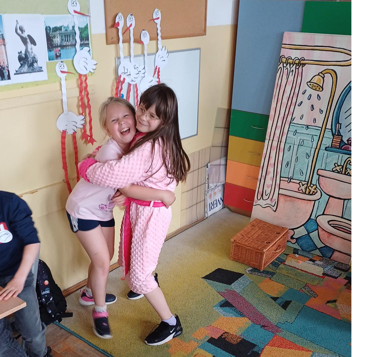 2 dziewczynki stoją w uścisku, w tle znajduje się makieta łazienki, 