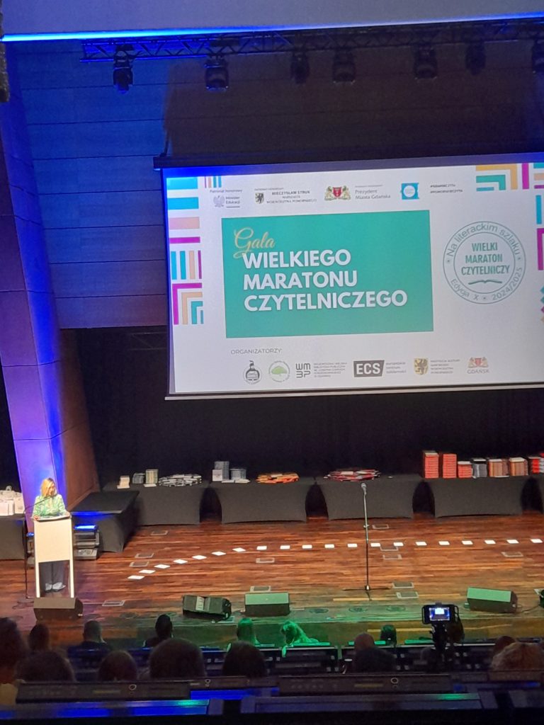 Zdjęcie przedstawia scenę z ekranem, na którym wyświetlono napis „Gala Wielkiego Maratonu Czytelniczego”