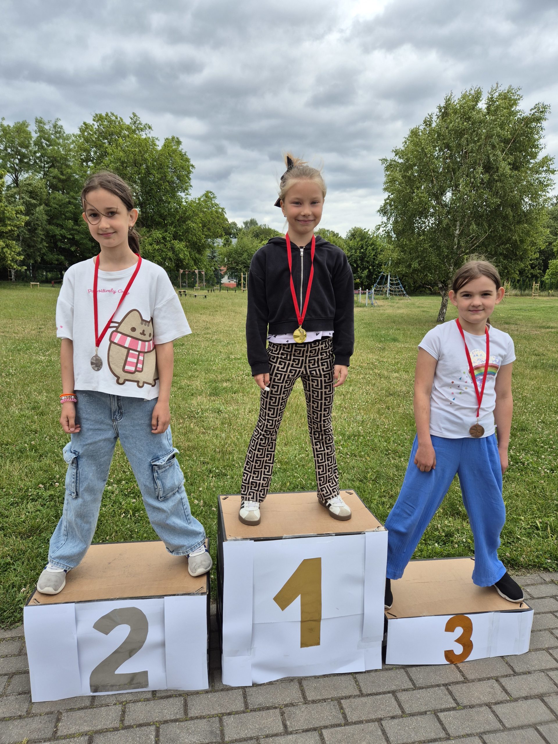 3 dziewczynki stoją na podium. Na szyi mają zawieszone medale.