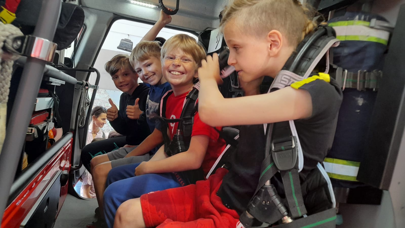 Czterech uśmiechniętych chłopców siedzi na przednich fotelach w wozie strażackim.