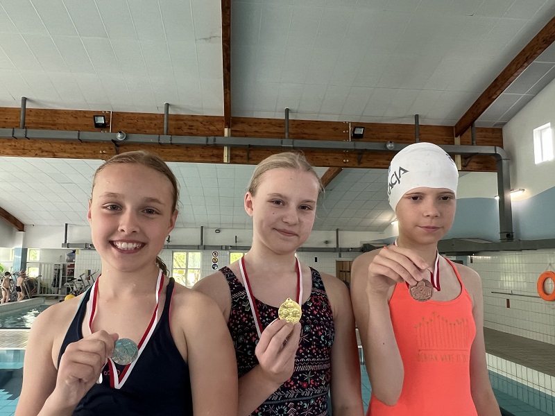 Trzy uczennice z medalami na piersiach pozują do zdjęcia