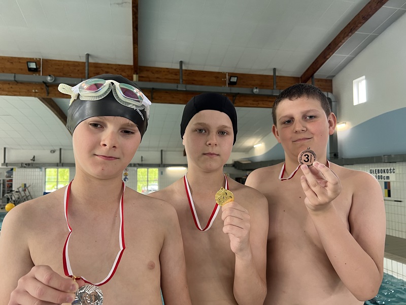 Trzech uczniów z medalami trzymanym w dłoniach pozuje do zdjęcia