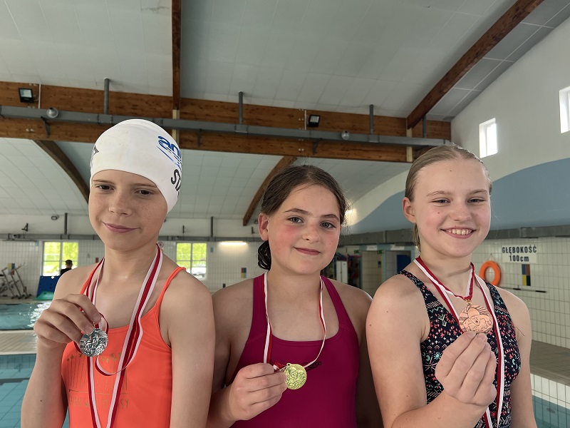 Trzy uczennice z medalami na piersiach pozują do zdjęcia