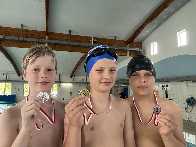 Trzech uczniów z medalami na piersiach pozują do zdjęcia