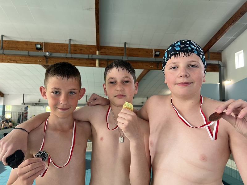 Trzech uczniów z medalami na piersiach pozują do zdjęcia