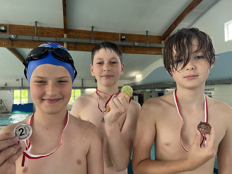 Trzech uczniów z medalami na piersiach pozują do zdjęcia