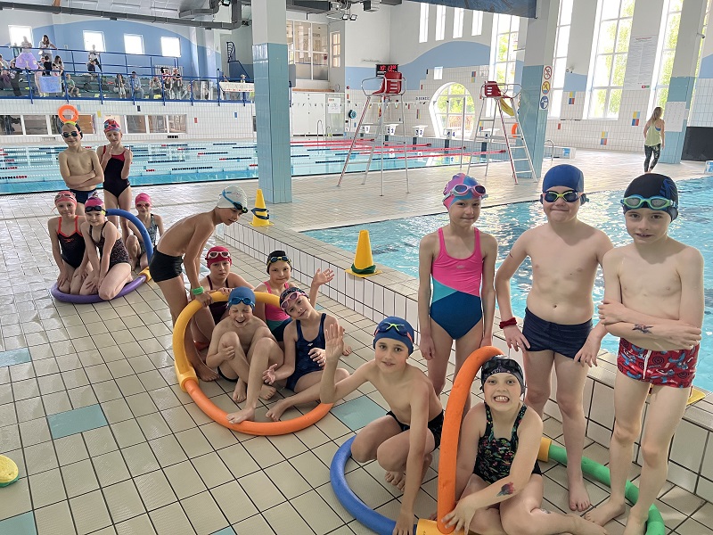 Po 5 uczniów przy tratwach wykonanych z makaronów i złączek pozuje do zdjęcia na tle basenu