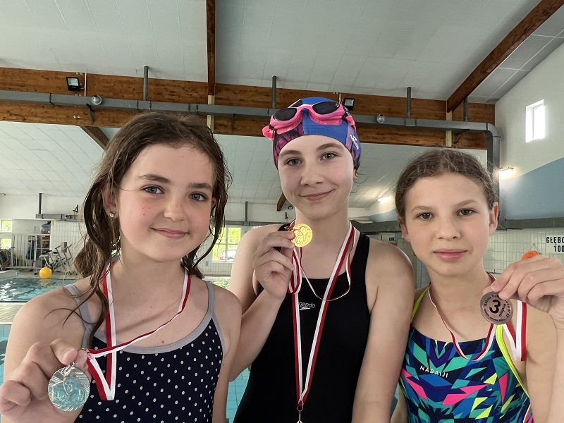 Trzy uczennice z medalami na szyi pozuje do zdjęcia