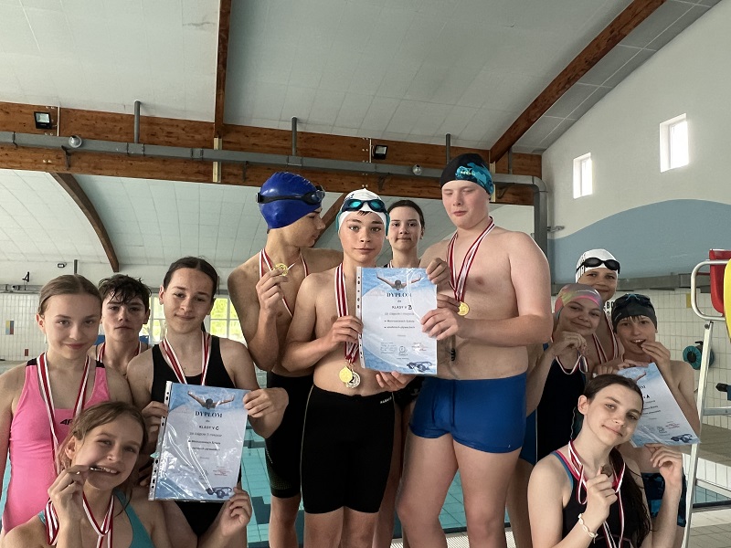 Uczniowie na 3 stopniach podium po 4 z każdej klasy z medalami na piersiach i dyplomem pozują do zdjęcia