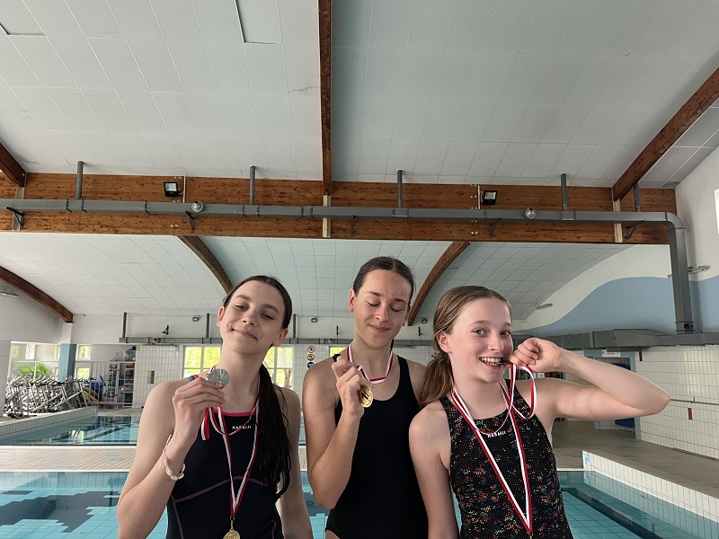 Trzy uczennice z medalami na piersiach pozują do zdjęcia