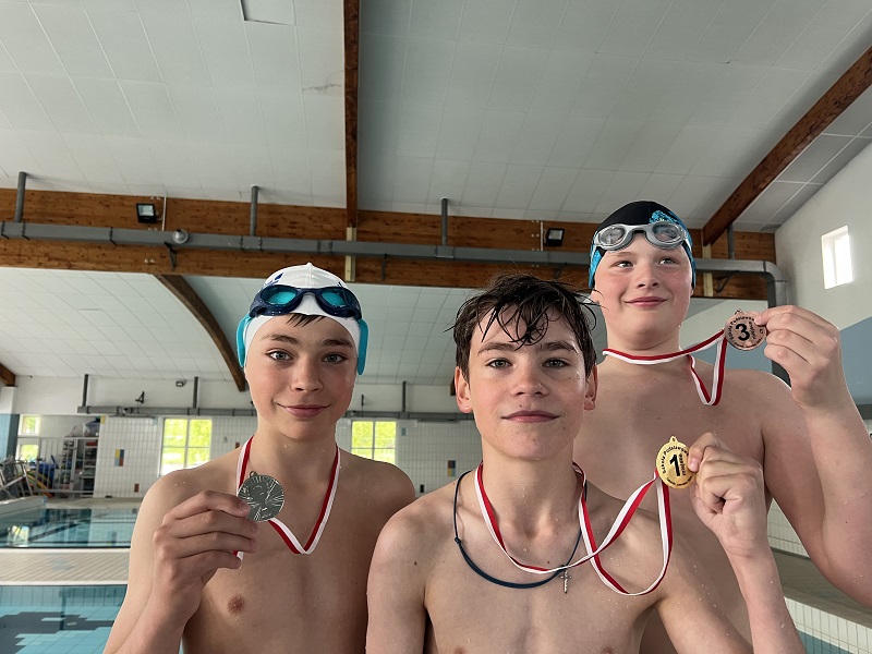 Trzech uczniów z medalami na piersiach pozują do zdjęcia