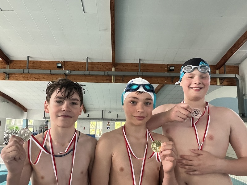 Trzech uczniów z medalami na piersiach pozują do zdjęcia
