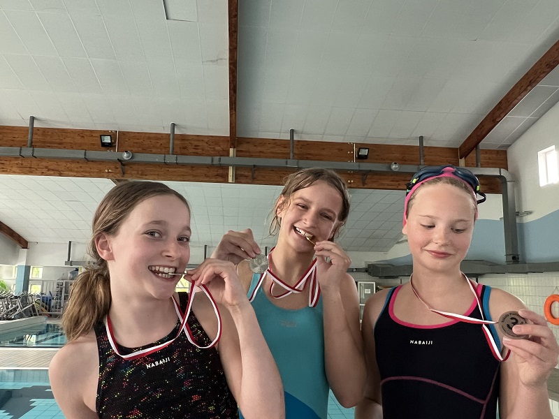 Trzy uczennice z medalami na piersiach pozują do zdjęcia