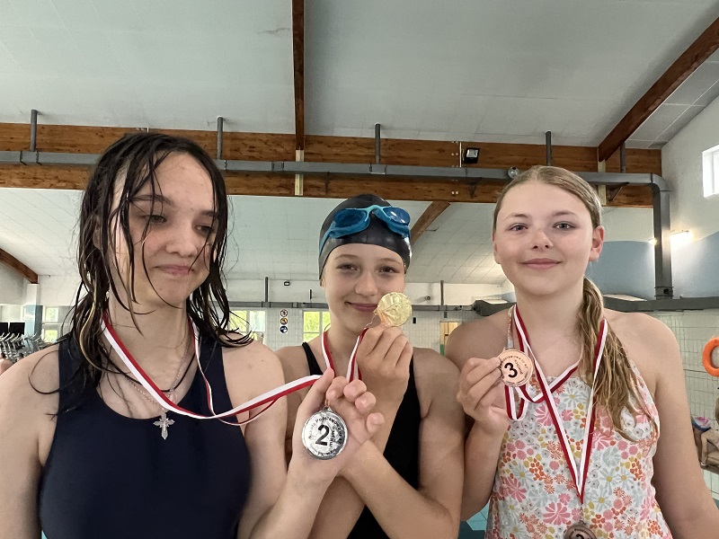 Trzy uczennice z medalami na piersiach pozują do zdjęcia