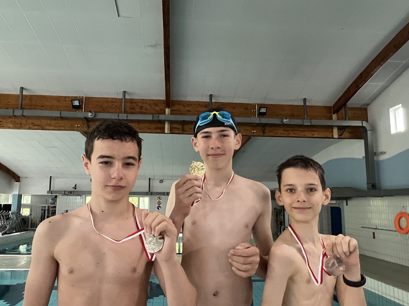 Trzech uczniów z medalami na piersiach pozują do zdjęcia