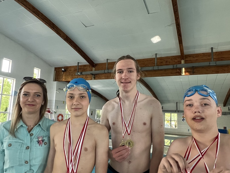 Trzech uczniów z medalami na szyi pozuje do zdjęcia z panią stojącą z lewej strony