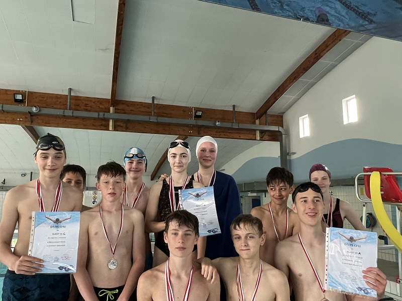 Uczniowie na 3 stopniach podium po 4 z każdej klasy z medalami na piersiach i dyplomem pozują do zdjęcia