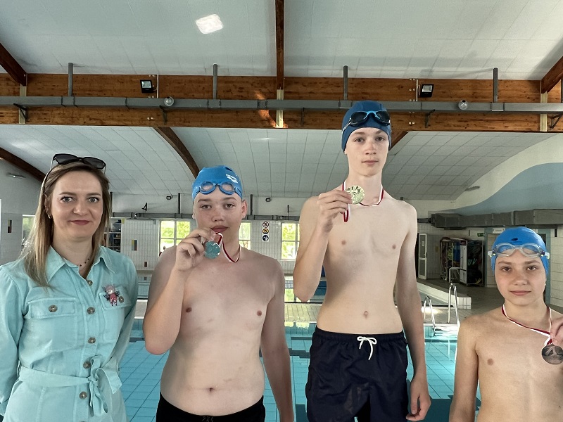 Trzech uczniów z medalami pozuje do zdjęcia z panią stojącą z lewej strony