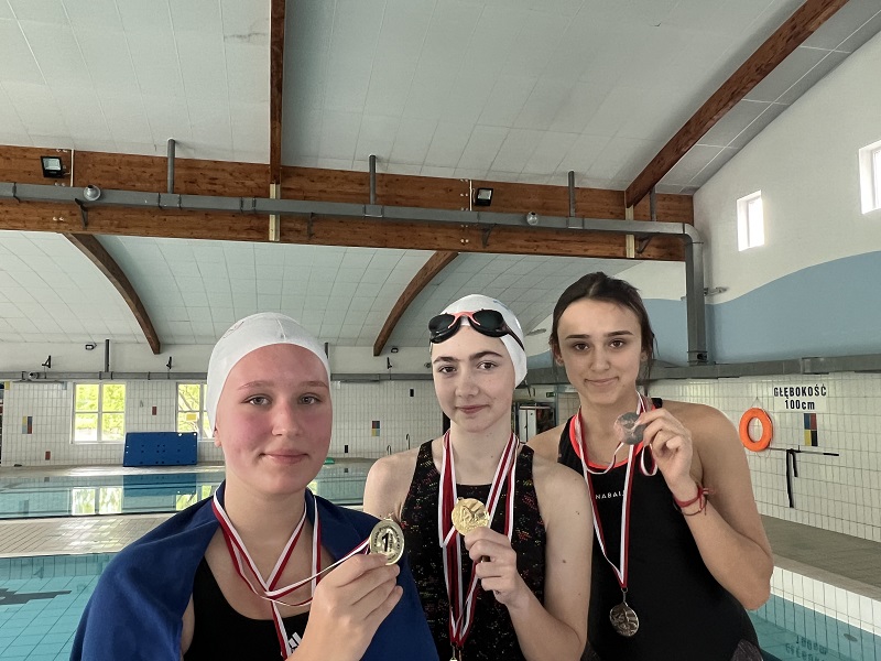 Trzy uczennice z medalami na piersiach pozują do zdjęcia