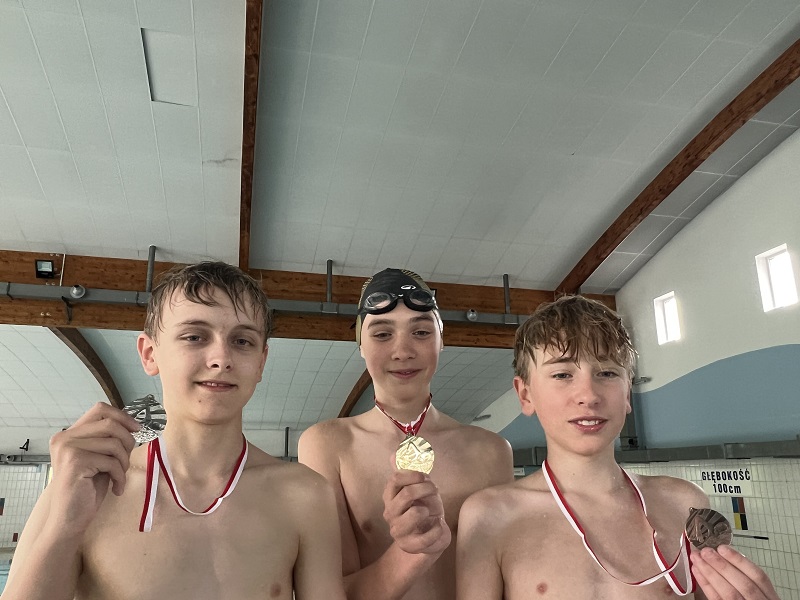 Trzech uczniów z medalami na piersiach pozują do zdjęcia