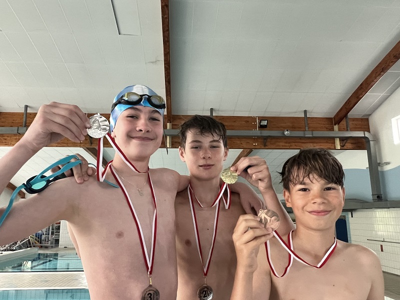 Trzech uczniów z medalami na piersiach pozują do zdjęcia