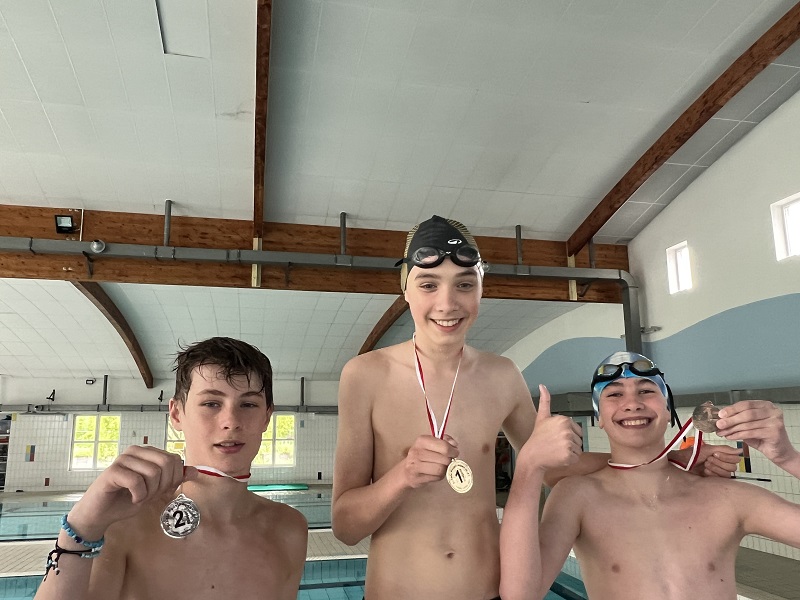 Trzech uczniów z medalami na piersiach pozują do zdjęcia