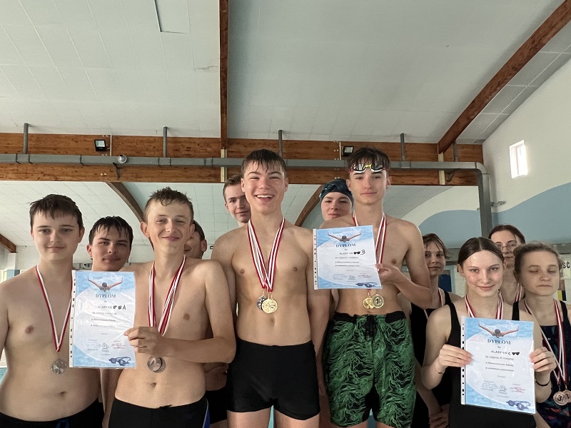 Uczniowie na 3 stopniach podium po 4 z każdej klasy z medalami na piersiach i dyplomem pozują do zdjęcia