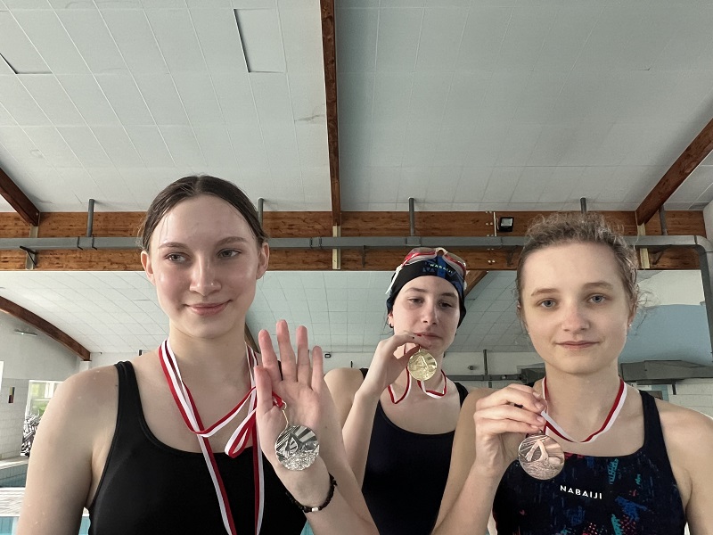 Trzy uczennice z medalami na piersiach pozują do zdjęcia