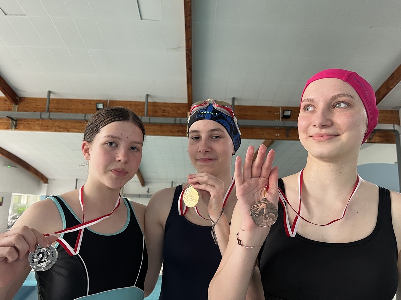Trzy uczennice z medalami na piersiach pozują do zdjęcia
