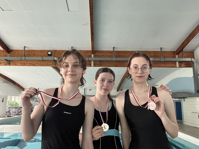 Trzy uczennice z medalami na piersiach pozują do zdjęcia