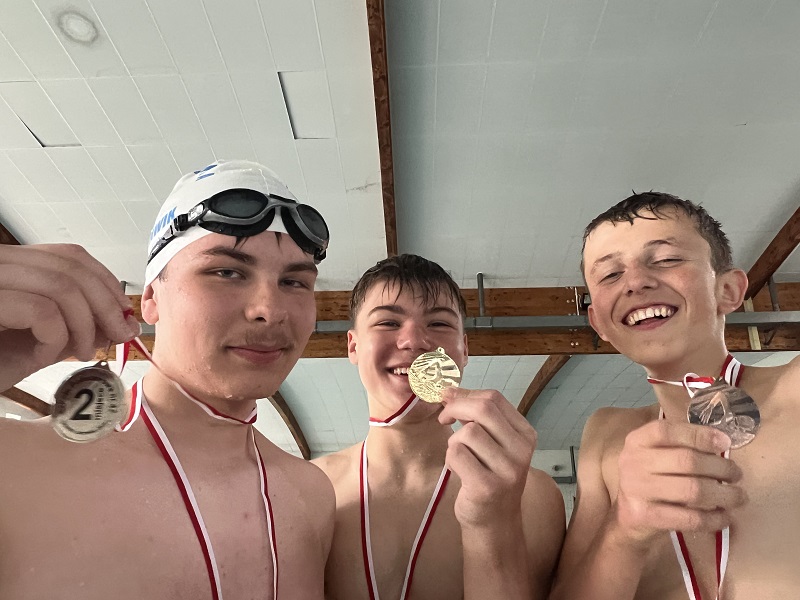Trzech uczniów z medalami na piersiach pozują do zdjęcia