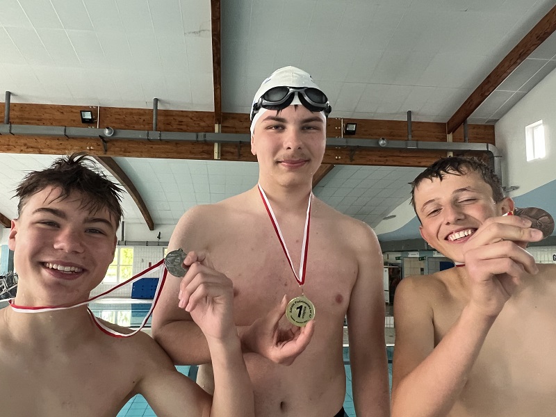 Trzech uczniów z medalami na piersiach pozują do zdjęcia