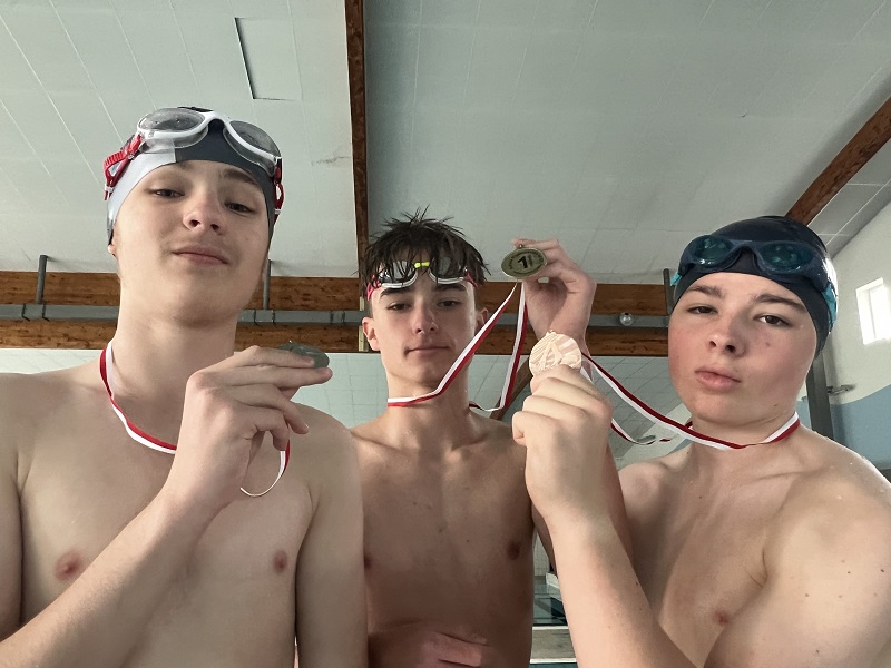 Trzech uczniów z medalami na piersiach pozują do zdjęcia